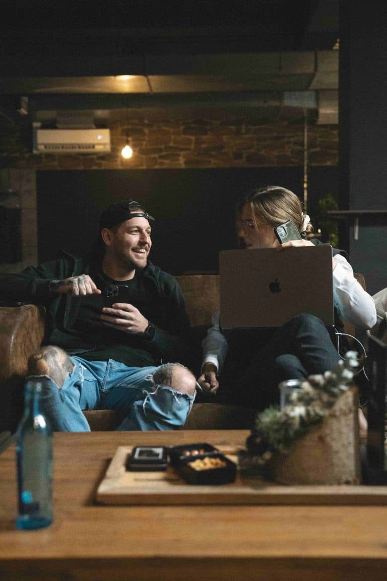 Zwei Personen sitzen entspannt auf einer Couch in der PIKASS Lounge, mit Laptop und Smartphone, bereit zum mobilen Arbeiten.