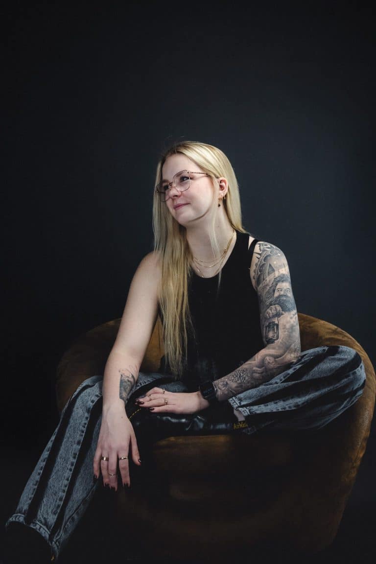Portrait von Josy (GOOSY), PIK ARTIST bei PIKASS Tattoo, mit detailreichen Tattoos am Arm, sitzend auf einem Sessel.