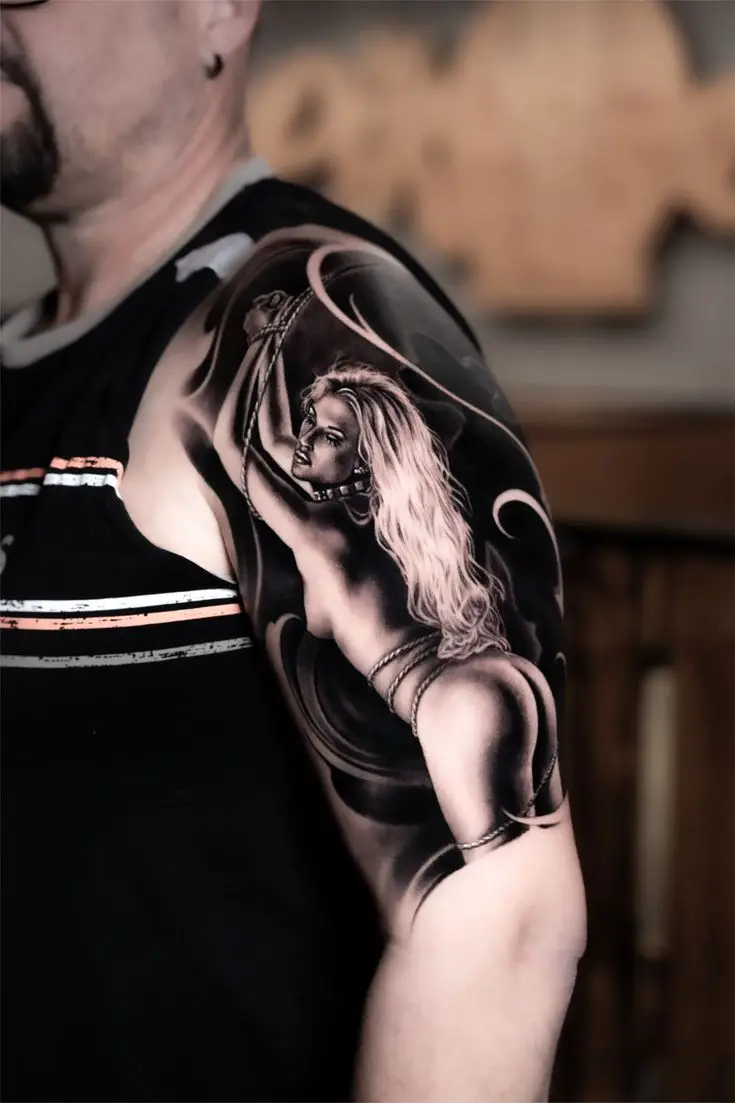Black and Grey Realism Tattoo am Oberarm mit Pin-up-Motiv, weichen Schattierungen und dunklem Hintergrund