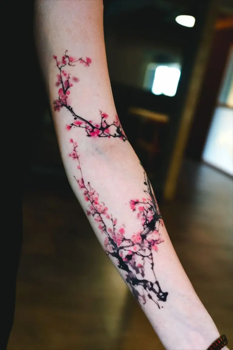 Farbiges Tattoo auf dem Unterarm mit Kirschblüten, schwarzen Ästen und roséfarbenen Brush-Style-Akzenten