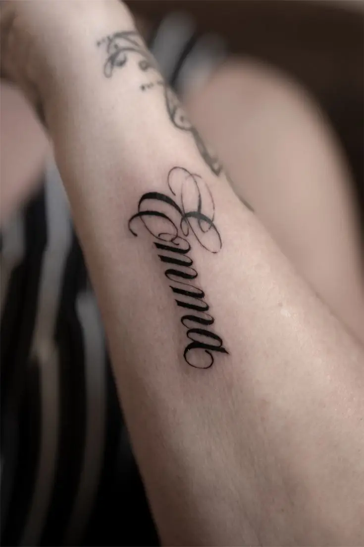 Feines Lettering Tattoo am Arm mit dem Schriftzug Amor und kleinem Herzdetail