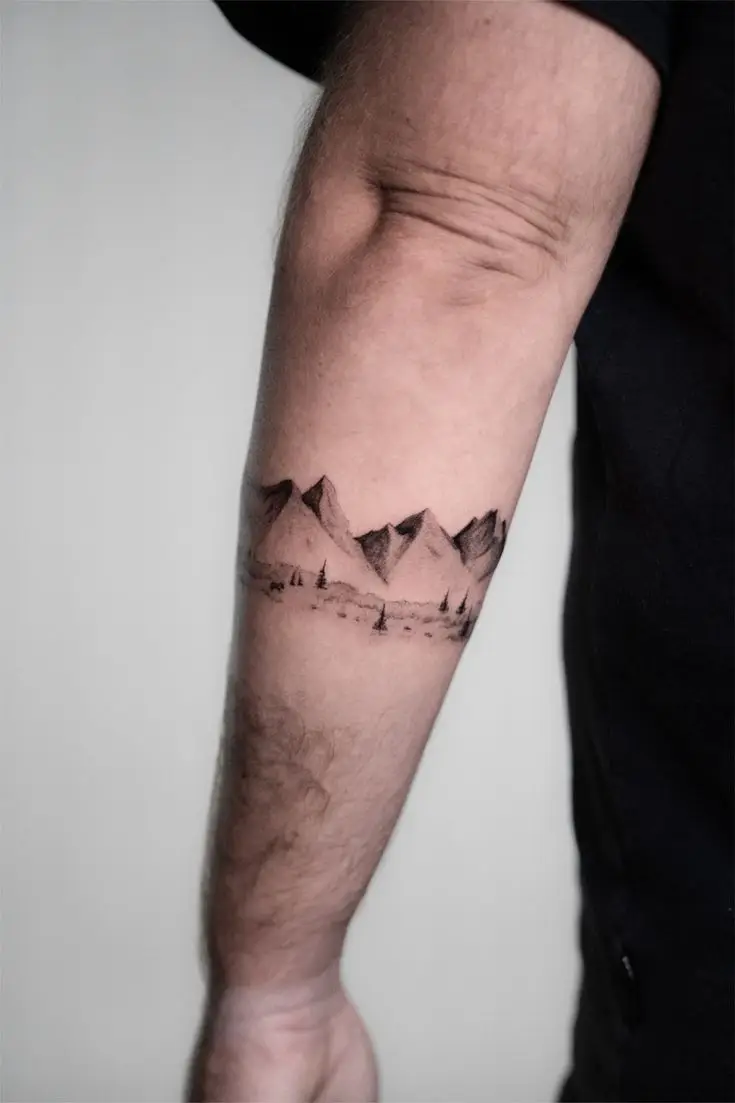 Feines Black-and-Grey-Tattoo mit Berglandschaft und kleinen Bäumen am Unterarm
