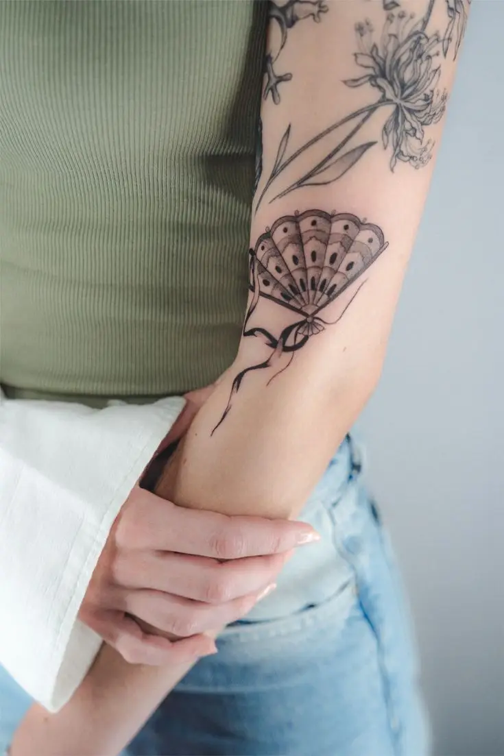Fineline-Tattoo mit dekorativem Fächer und floralen Elementen am Arm