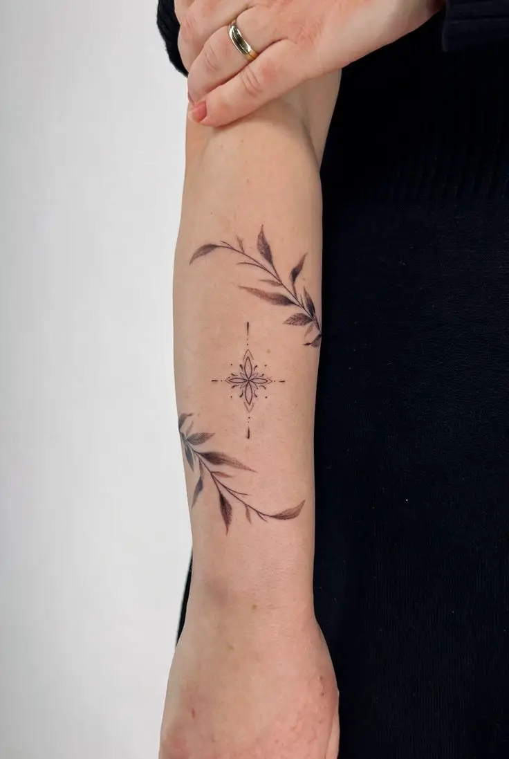 Ornamentales Fineline-Tattoo mit Blüten und geschwungenen Blättern am Unterarm