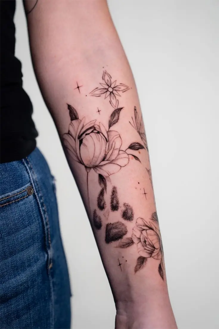 Fineline-Tattoo mit Pfotenabdruck, Blumen, Blättern und kleinen Sternen am Unterarm